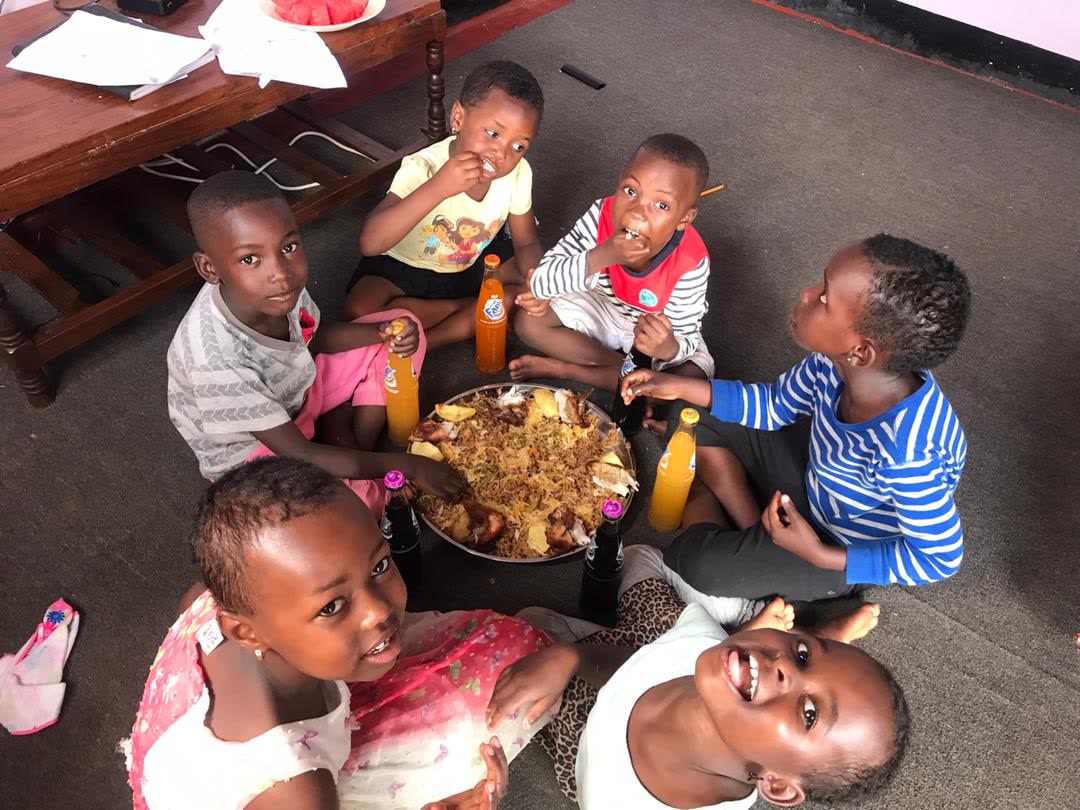 Children at the home sitting together on the floor, eating a meal.
