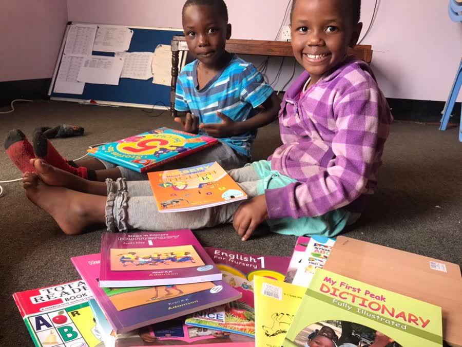 Two children sitting on the floor behind a spread of new school textbooks.