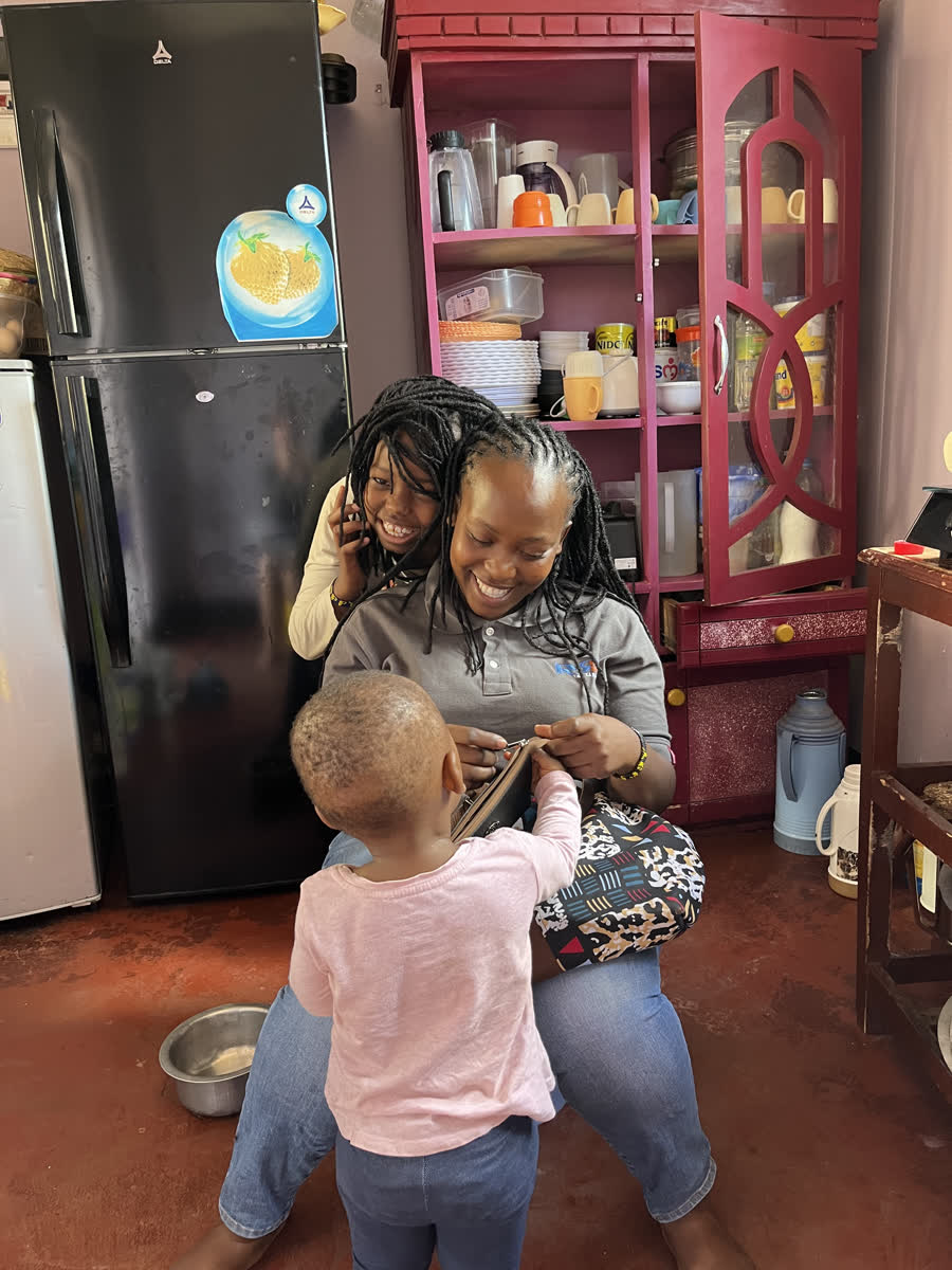 The kitchen at the home, with staff and a small child by the pink shelves.