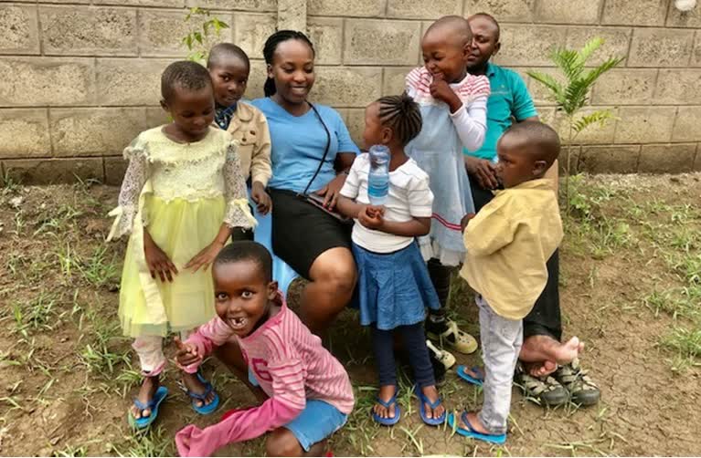 A member of staff sitting outside surrounded by the children.
