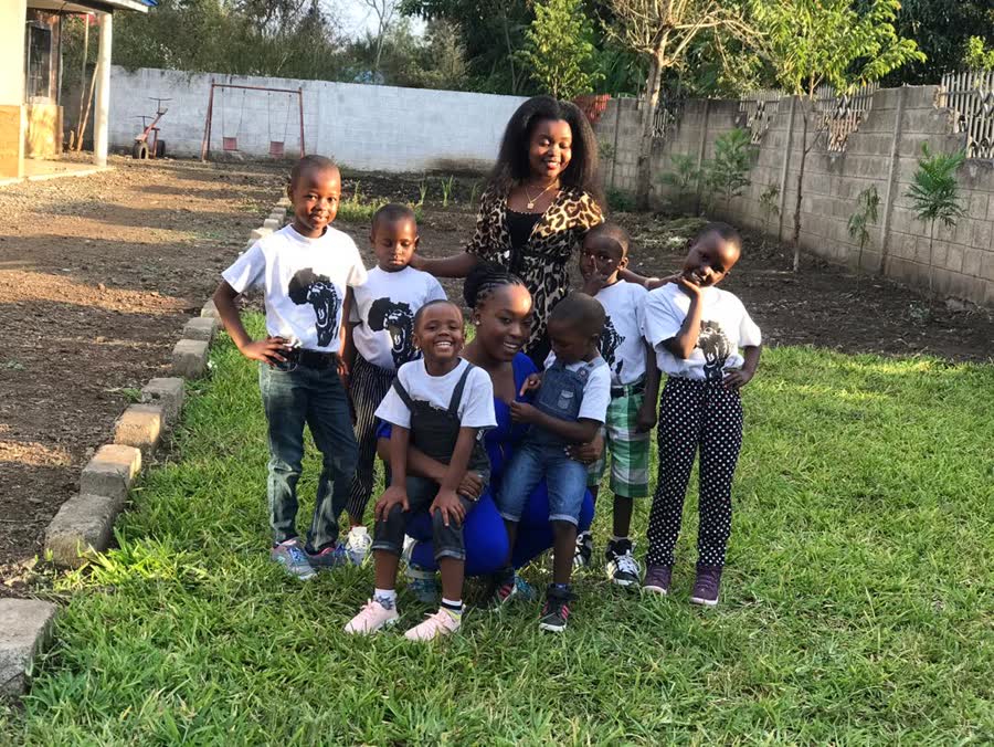 Children of the home in matching Africa tee-shirts on the grass with two members of staff, everyone smiling at the camera.