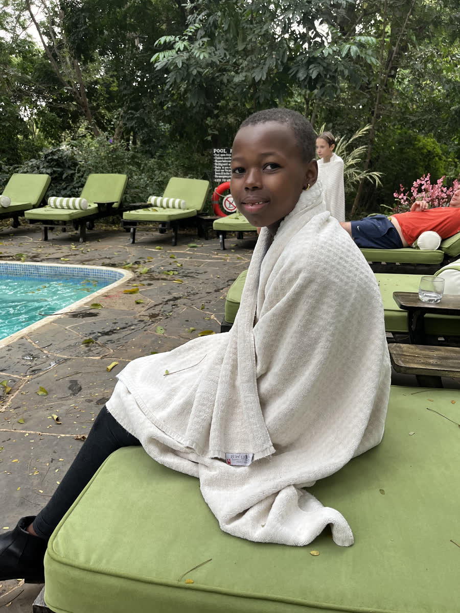 A girl wrapped in a towel sitting beside the pool.