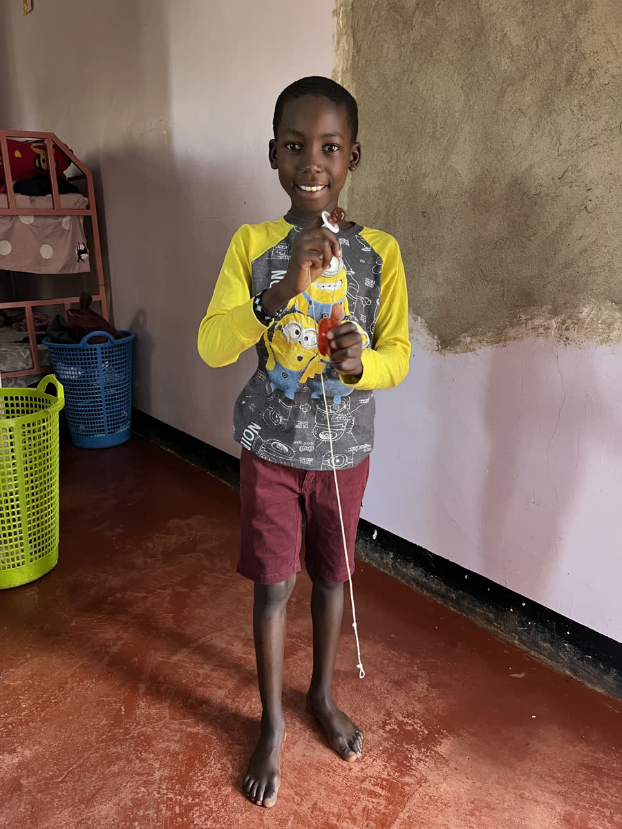 A boy standing in the dormitory holding up a yo-yo on its string.