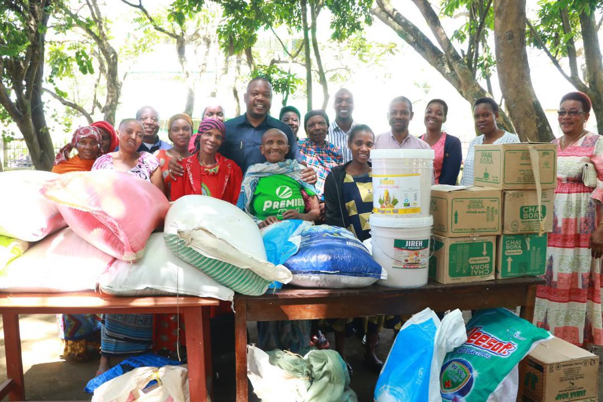 Sacks of maize, cooking oil, tea and soap laid out on tables, with the group gathered behind them.