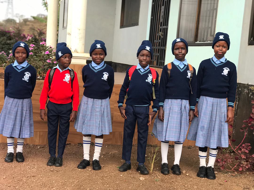 Six children from the home standing outside in navy school uniforms and hats with backpacks, ready for school.